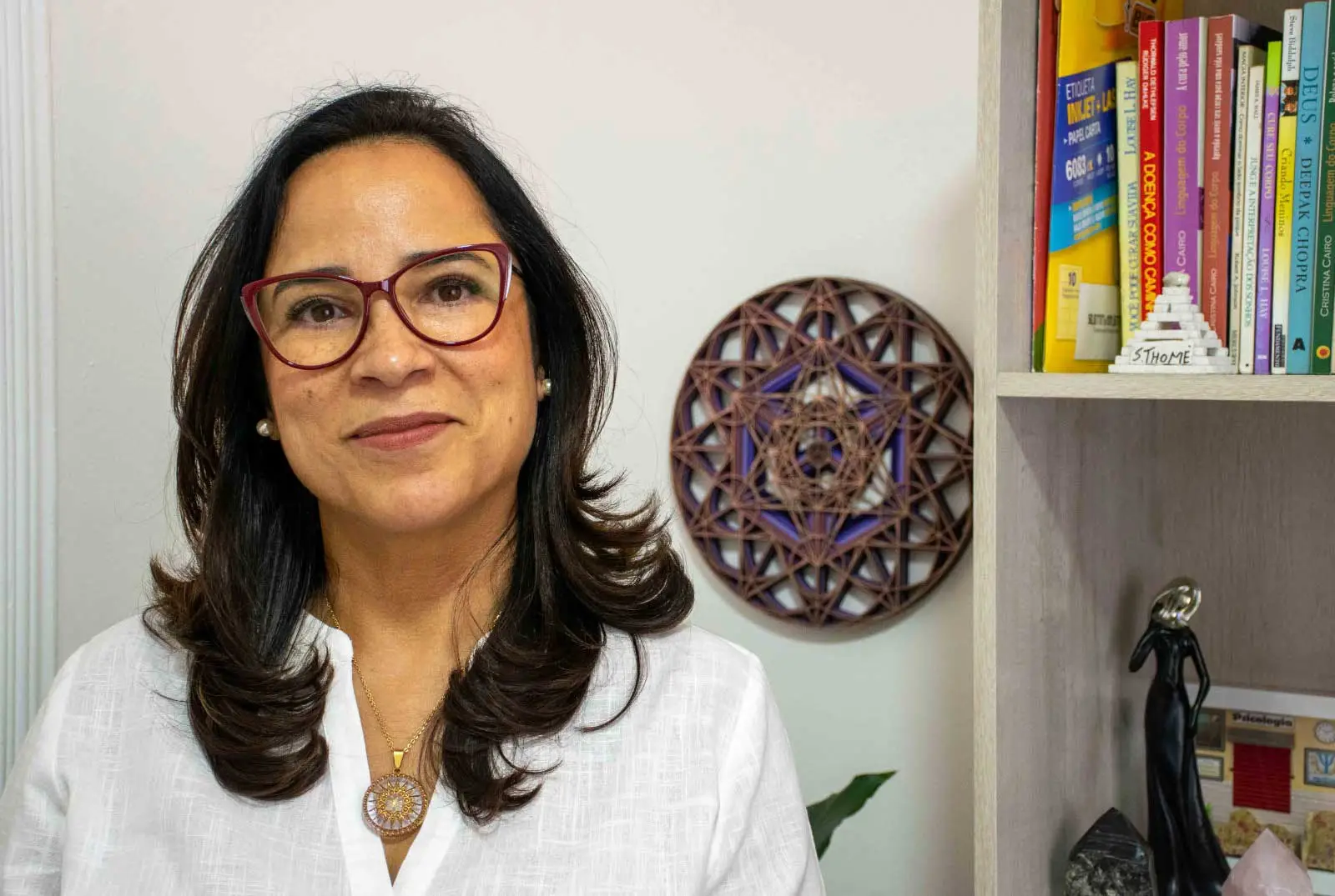 Gislene Xavier, psicóloga clínica, em ambiente de atendimento com livros ao fundo.
